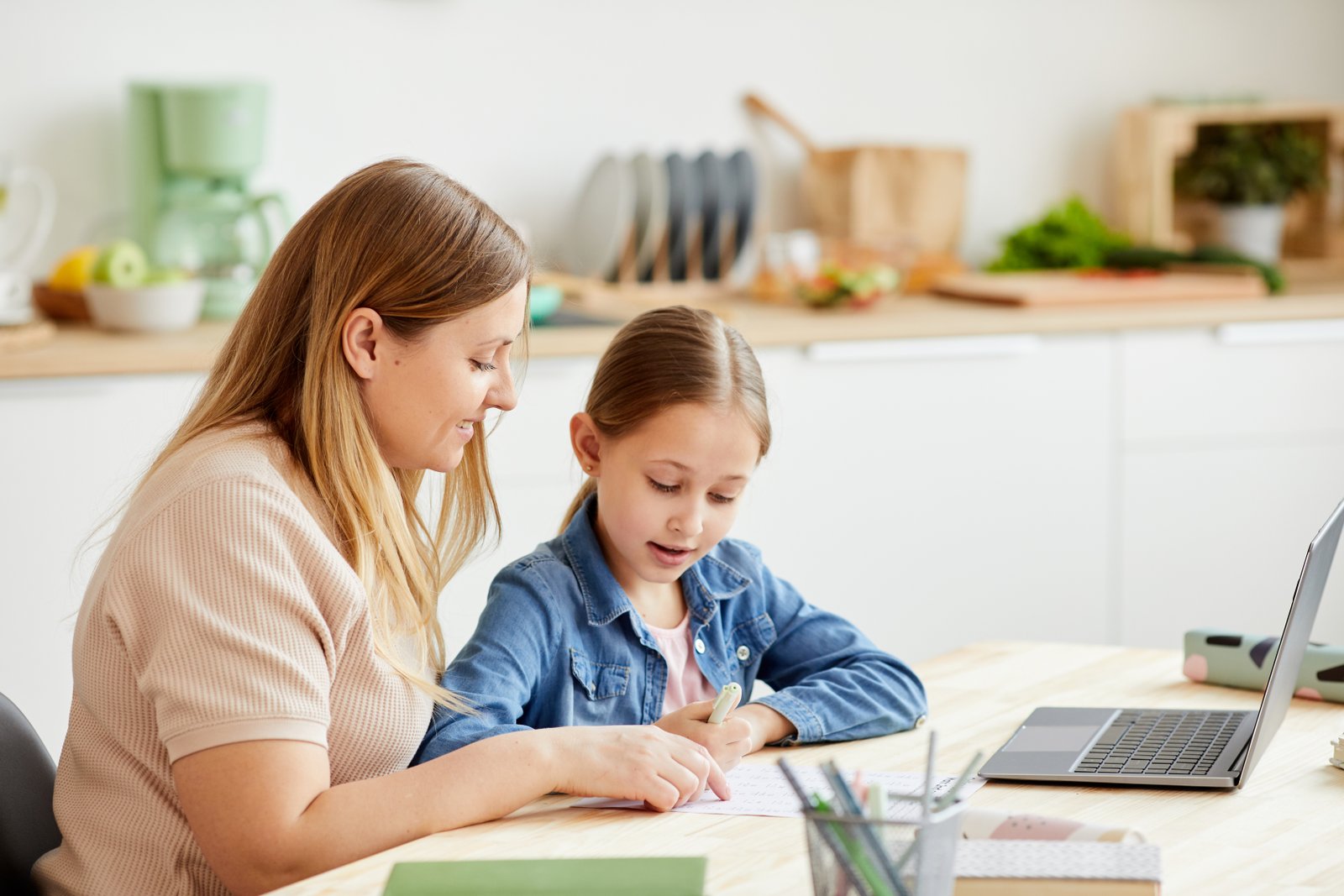 Parent supporting a child with home learning at the kitchen table