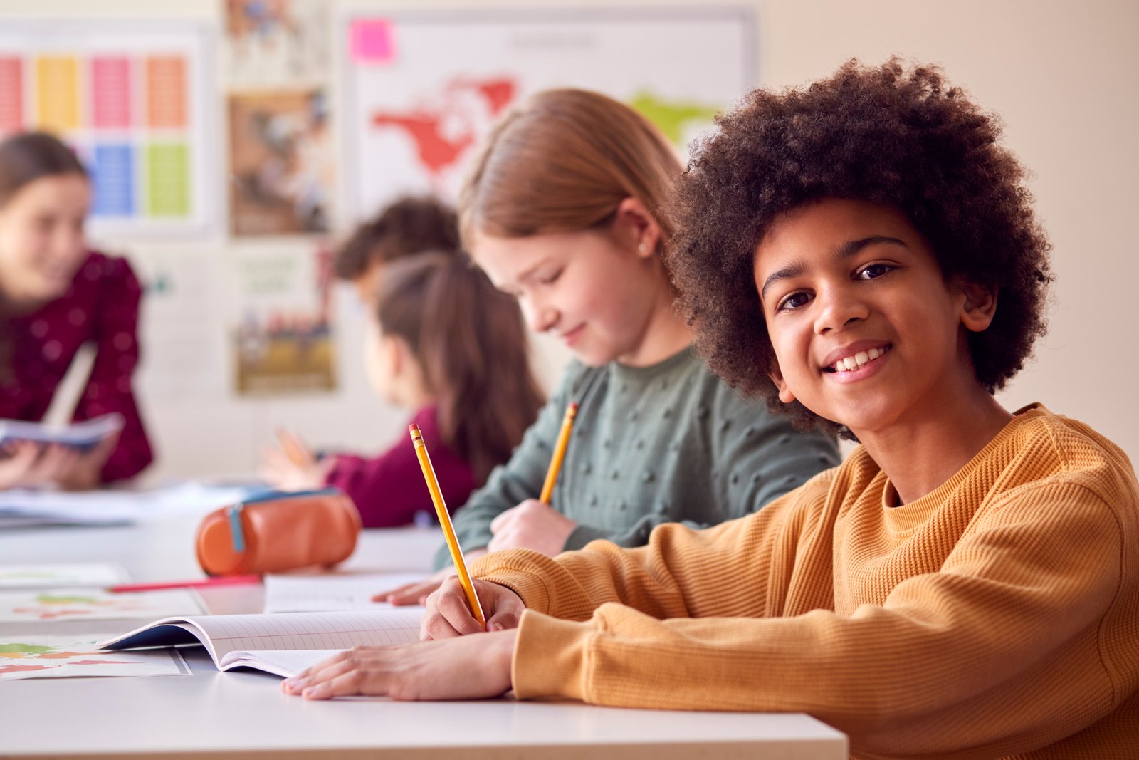 Smiling primary student working at a desk with teacher support in the classroom